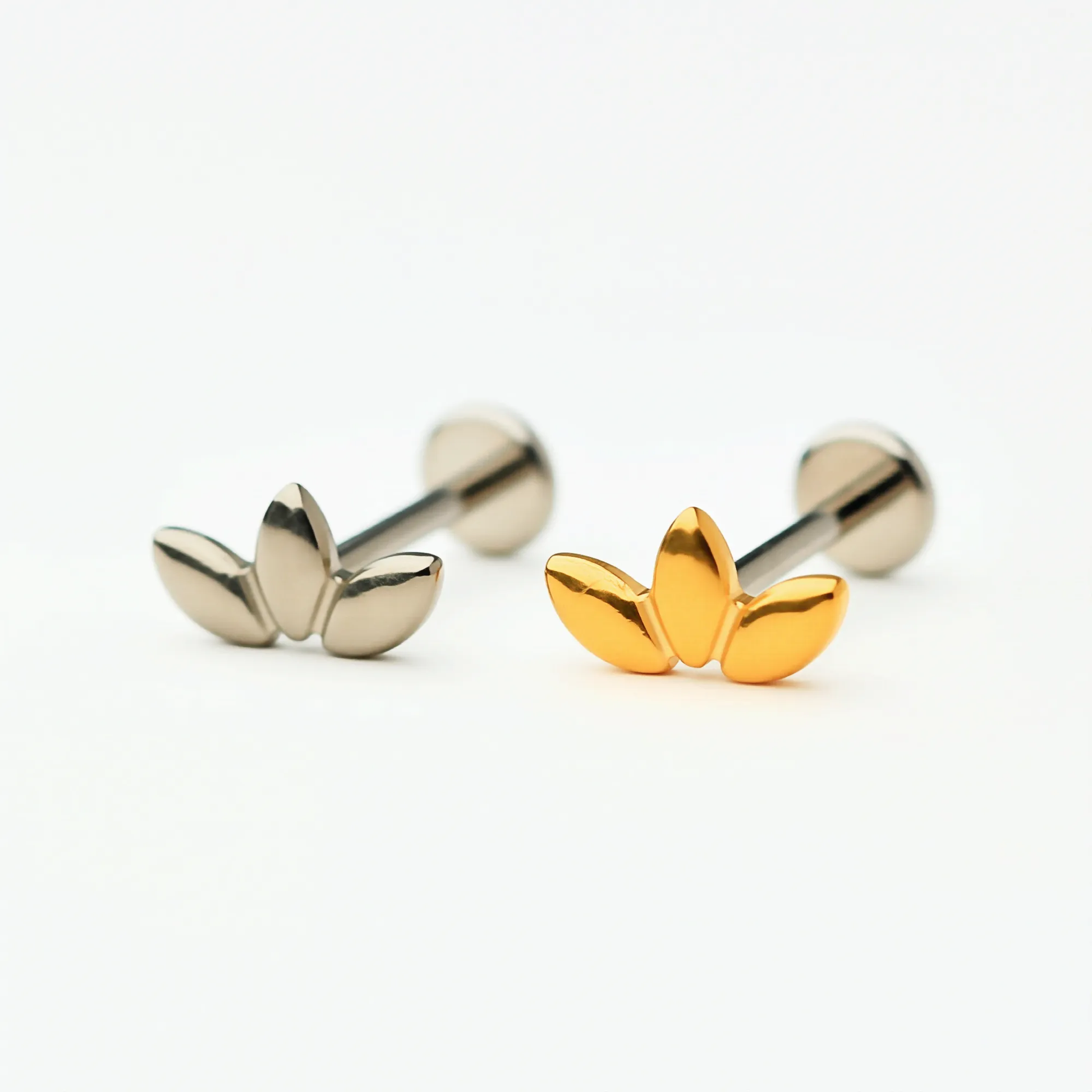Titanium Triple Leaf flat back stud earrings in natural titanium and gold, featuring a three-petal leaf design. Front view showing hypoallergenic implant-grade titanium push-in posts and flat back style.