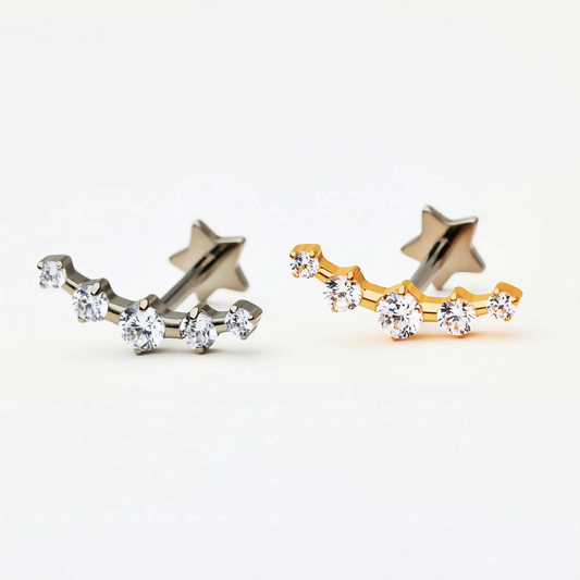 Titanium Radiant Row internally threaded flat back stud earrings in natural titanium and gold, featuring a star detail and a row of sparkling crystals. Front view of hypoallergenic implant-grade titanium studs.