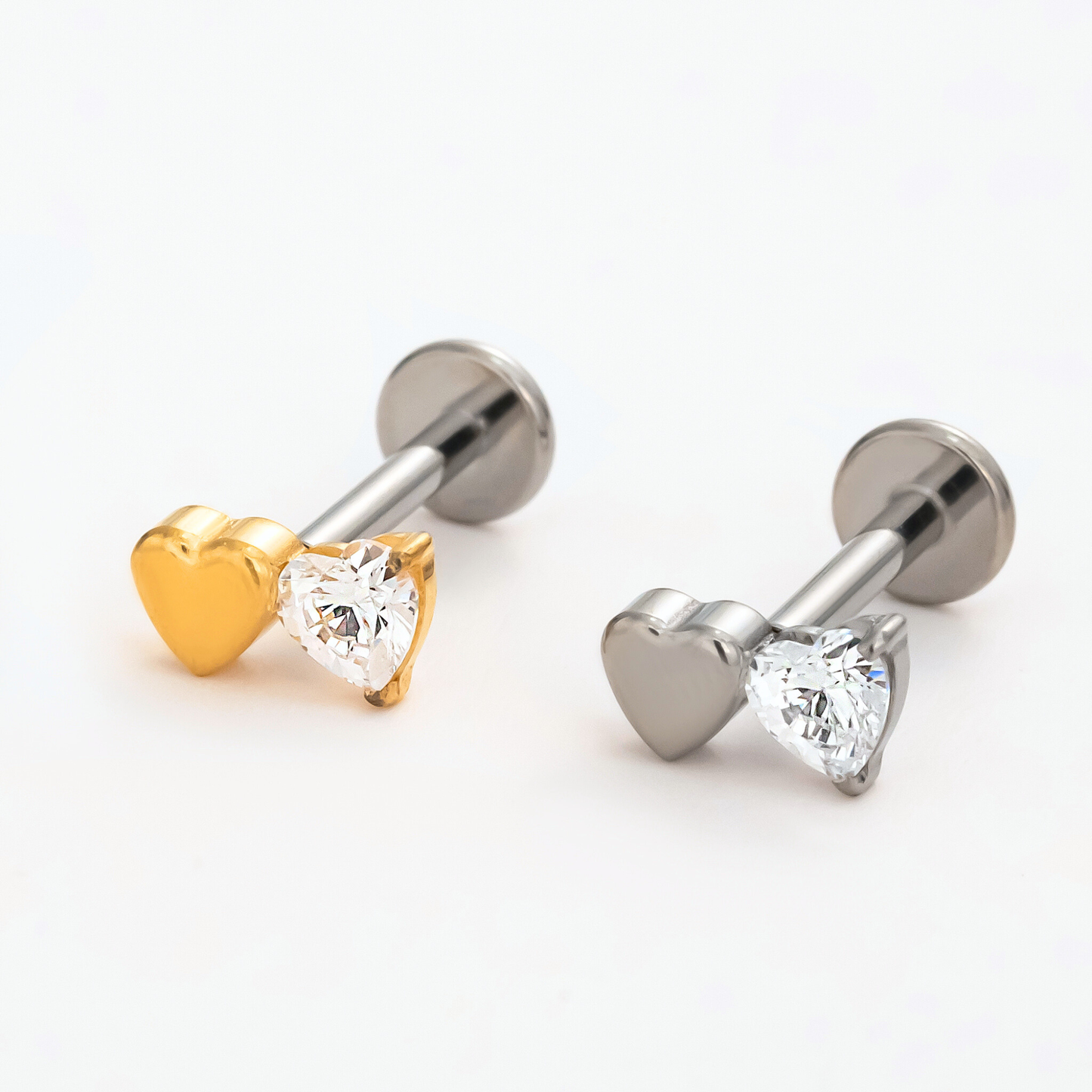 Titanium Duo Heart internally threaded flat back stud earrings in natural titanium and gold, featuring a metal heart paired with a clear crystal heart. Front view of hypoallergenic implant-grade titanium studs.