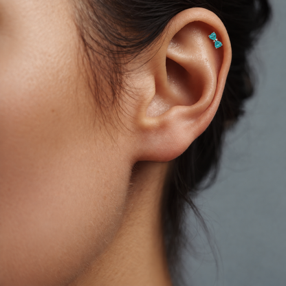 Heart Bow titanium earring with teal heart-shaped CZ stones, worn on the helix